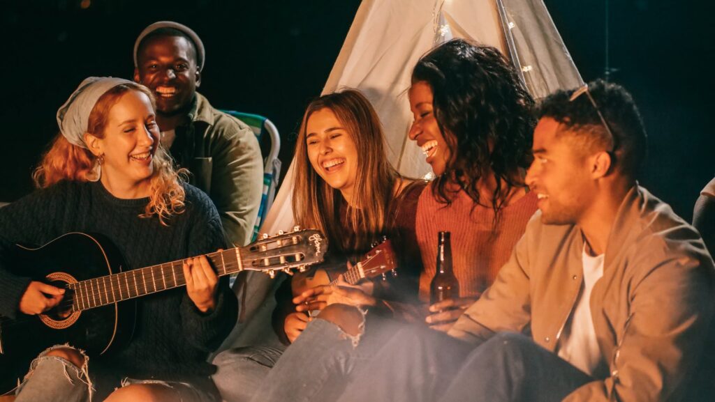 group of friends singing while sitting on beach sand