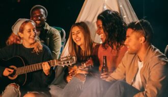 group of friends singing while sitting on beach sand